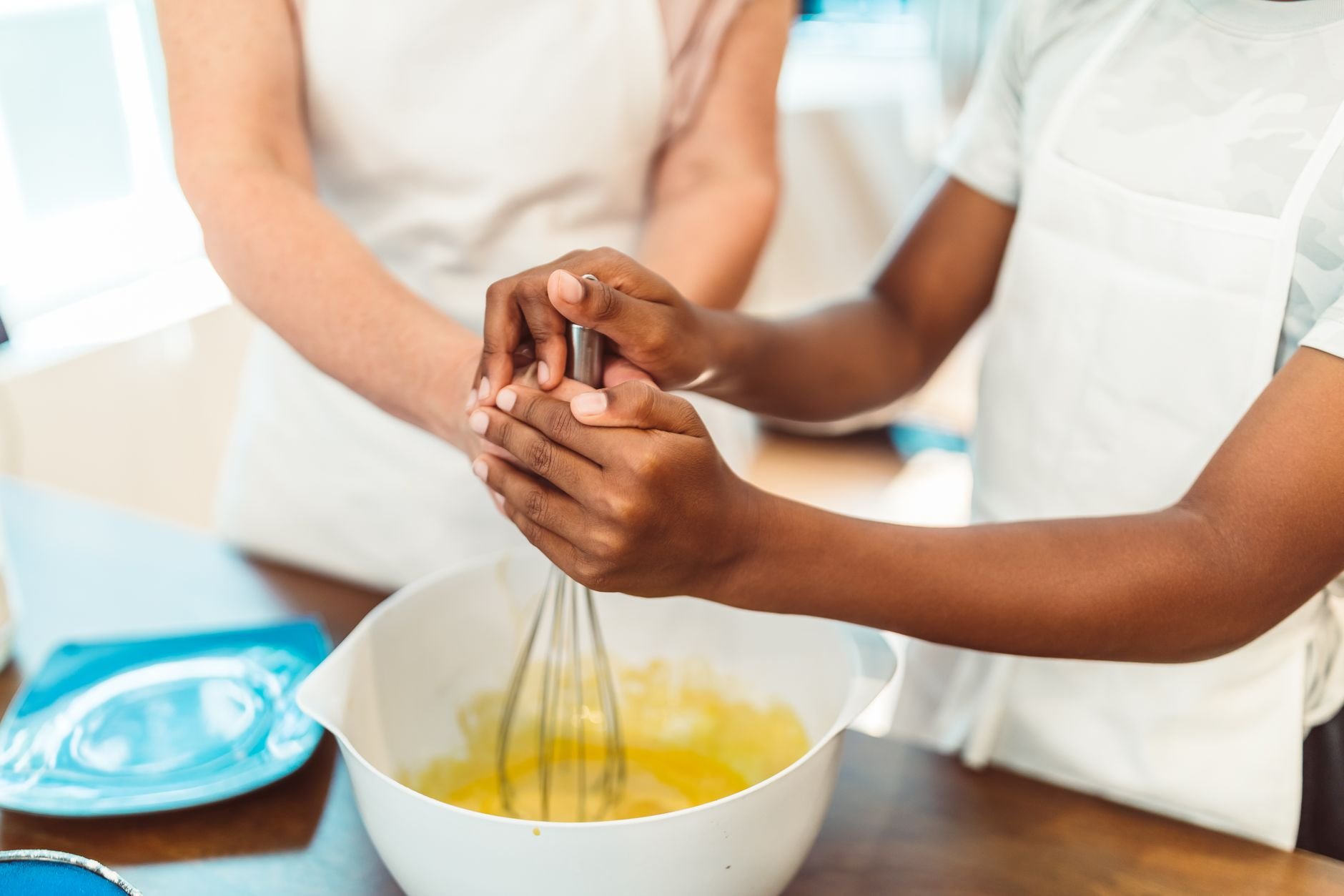 Close-up of hands working together to mix ingredients in a white bowl during a cooking session.